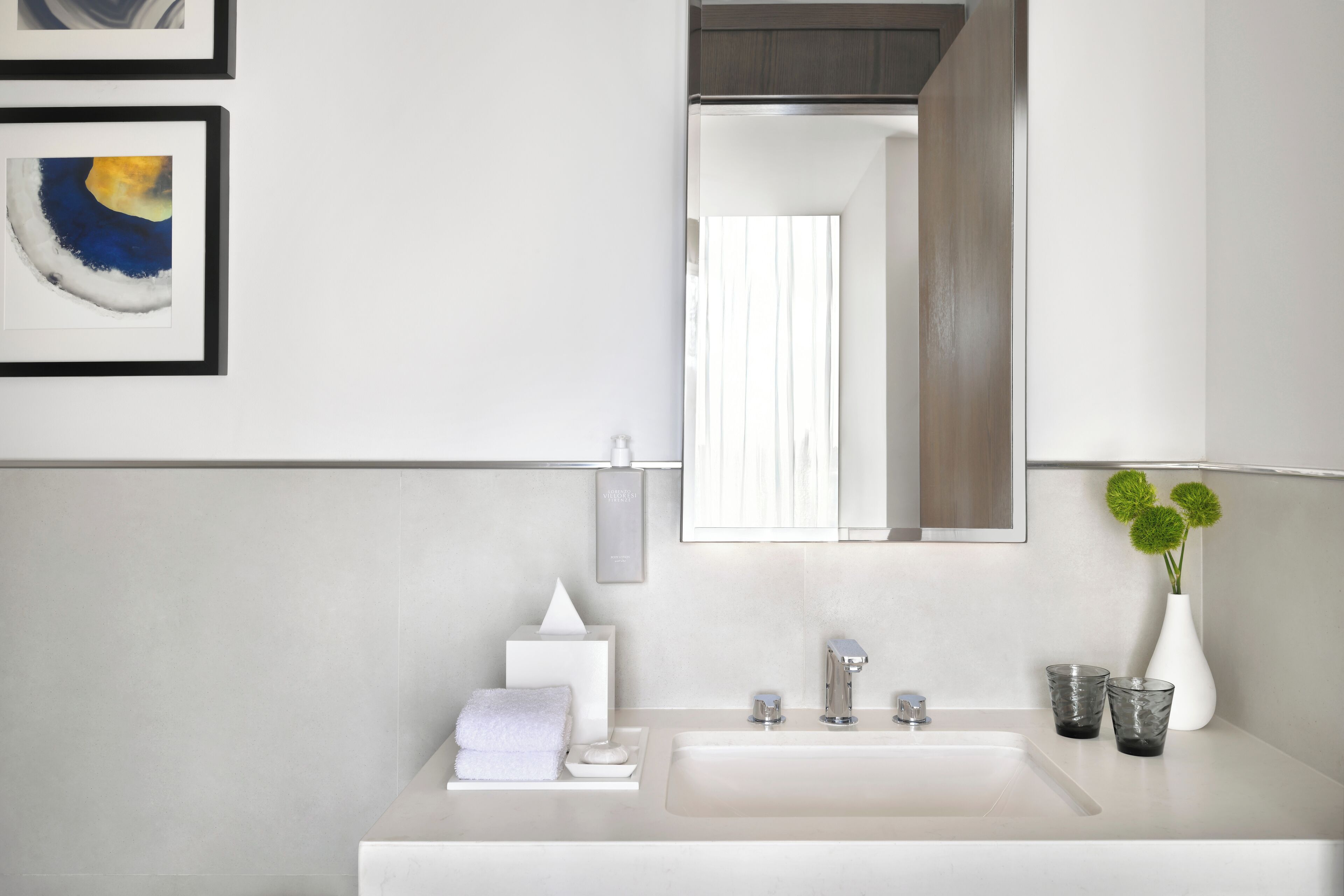 A modern bathroom with a white sink, a mirror, a towel, a soap dispenser, and a glass of water.