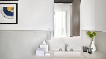 A modern bathroom with a white sink, a mirror, a towel, a soap dispenser, and a glass of water.