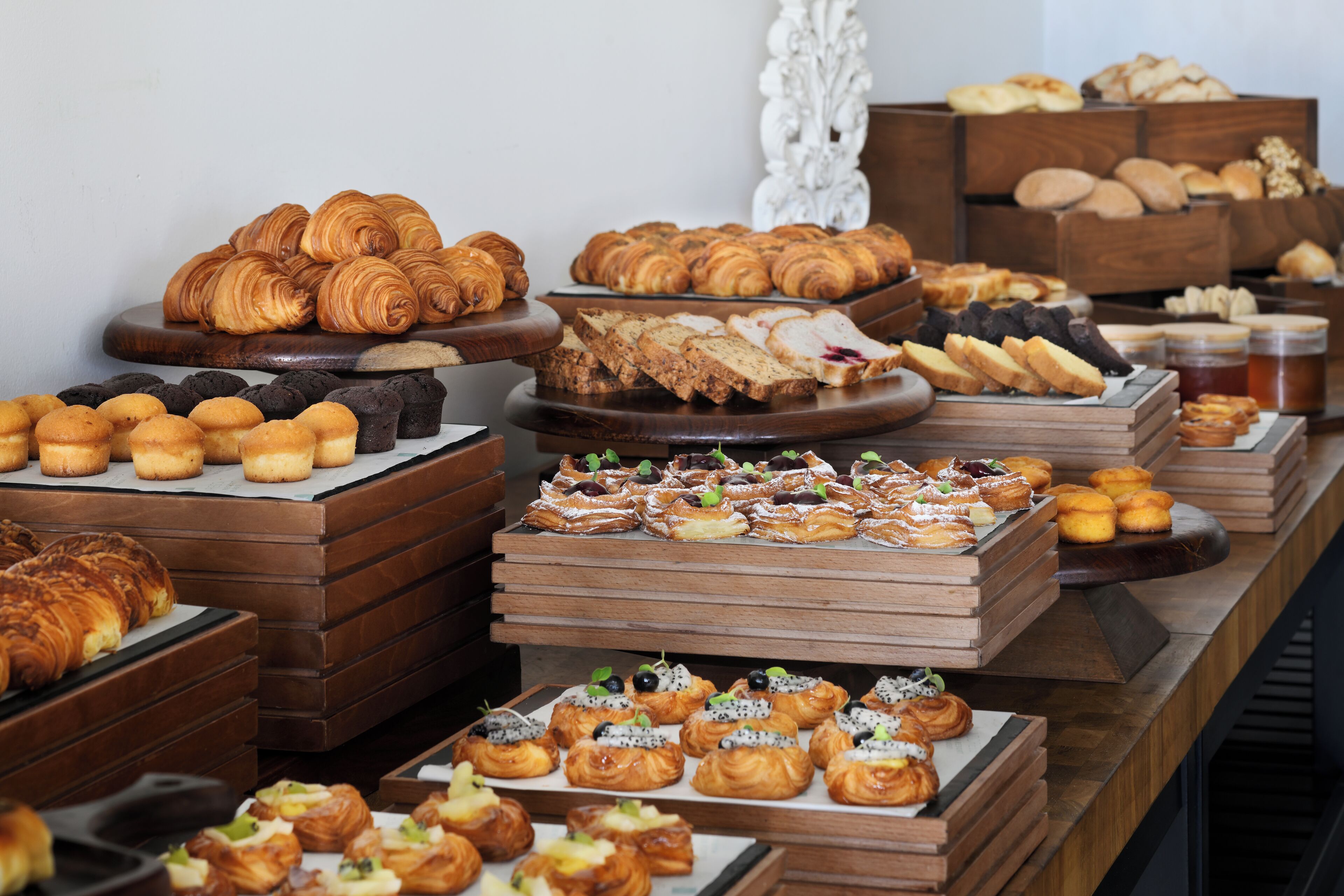 A variety of pastries and baked goods displayed on wooden stands and trays.