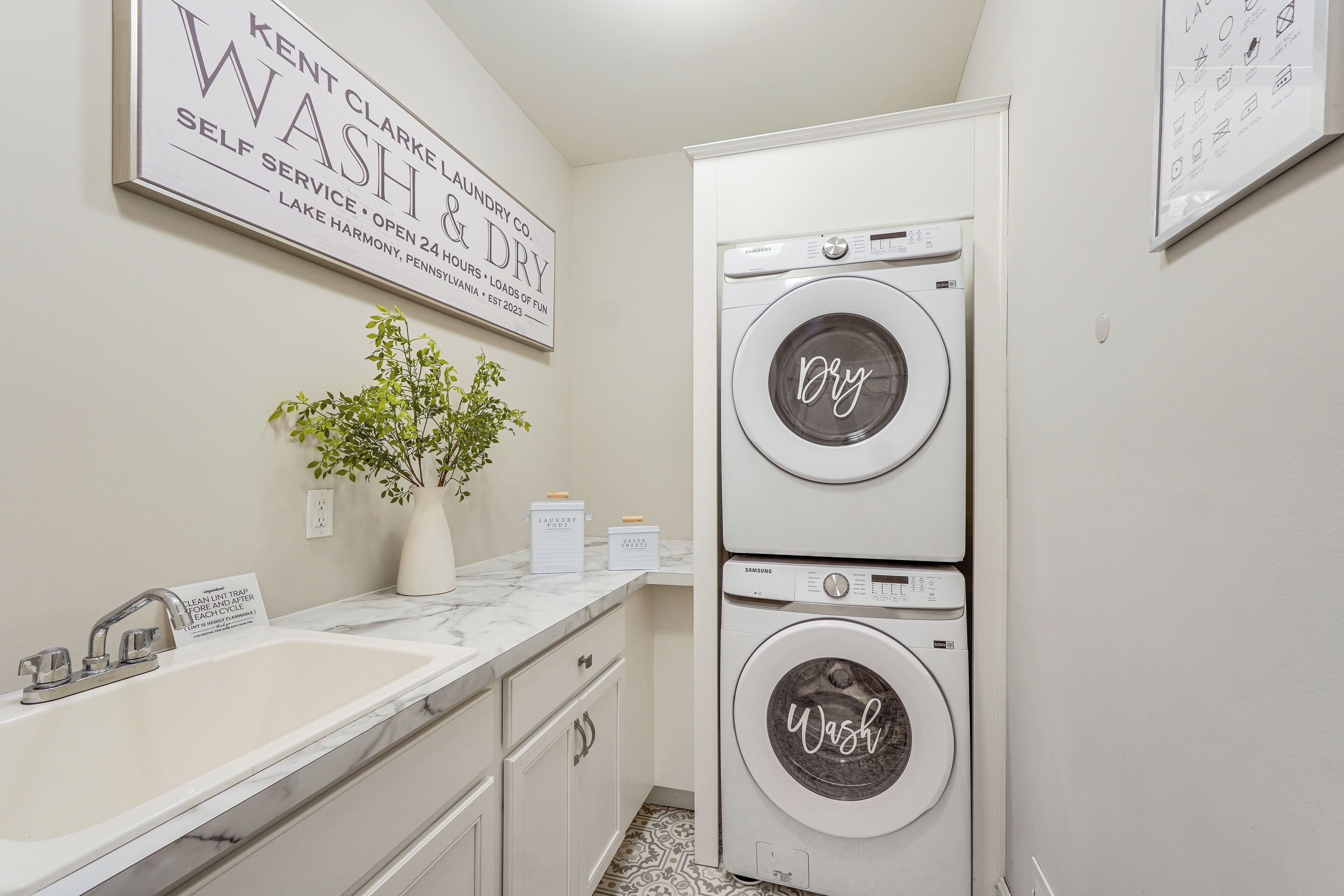 A laundry room with two stacked washers and dryers, a sink, and a potted plant.