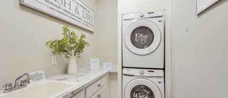 A laundry room with two stacked washers and dryers, a sink, and a potted plant.