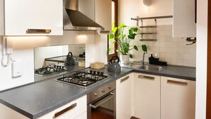 A modern kitchen with a gas stove, white cabinets, a stainless steel range hood, and a potted plant. - Torretta Arena Verona (Verona)
