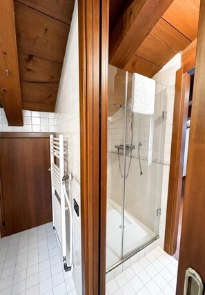 Un baño moderno con cabina de ducha de vidrio, paredes de azulejos blancos y vigas de madera en el techo.