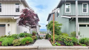 A residential street with two-story houses, a concrete pathway, and various plants. - Snoqualmie Townhome w/ Balcony & Mountain Views! (Snoqualmie)