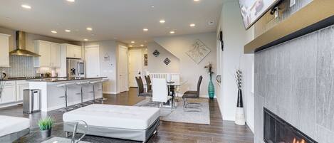 A modern living room with a fireplace, a dining area, and a kitchen.