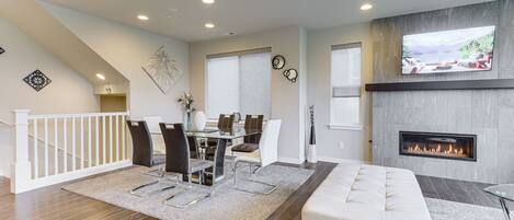 A modern living room with a fireplace, a dining area, and a staircase.