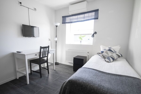 A bedroom with a bed, a desk, a chair, a TV, a window, and a radiator. - Brink Annex (Esl öv)
