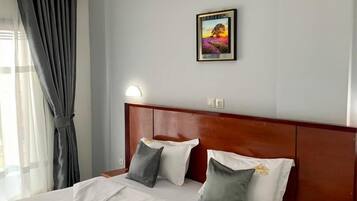 A hotel room with a neatly made bed, a wooden headboard, a bedside table with a phone, and a painting on the wall.