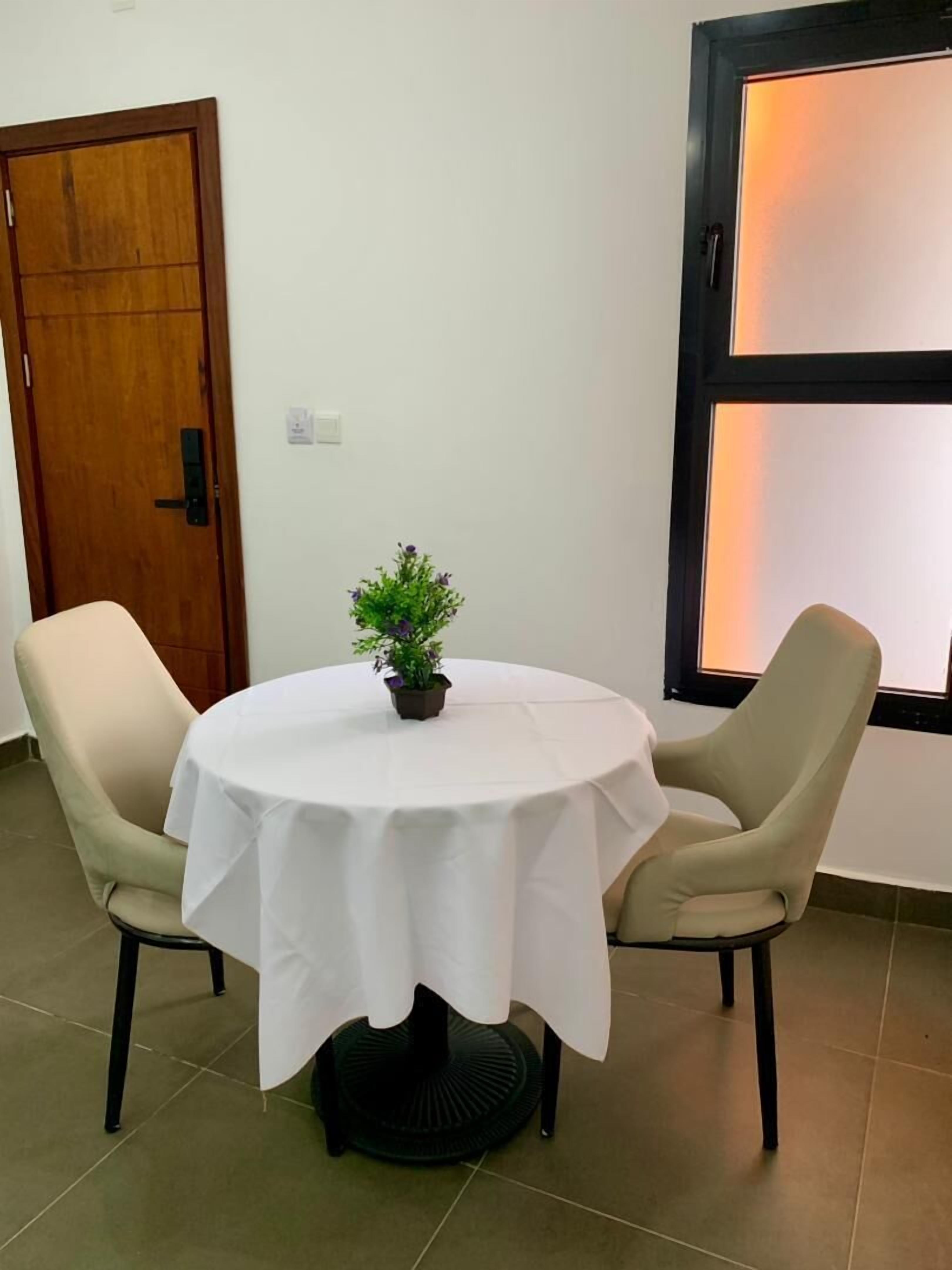 A round table with a white tablecloth, two beige chairs, and a small potted plant.