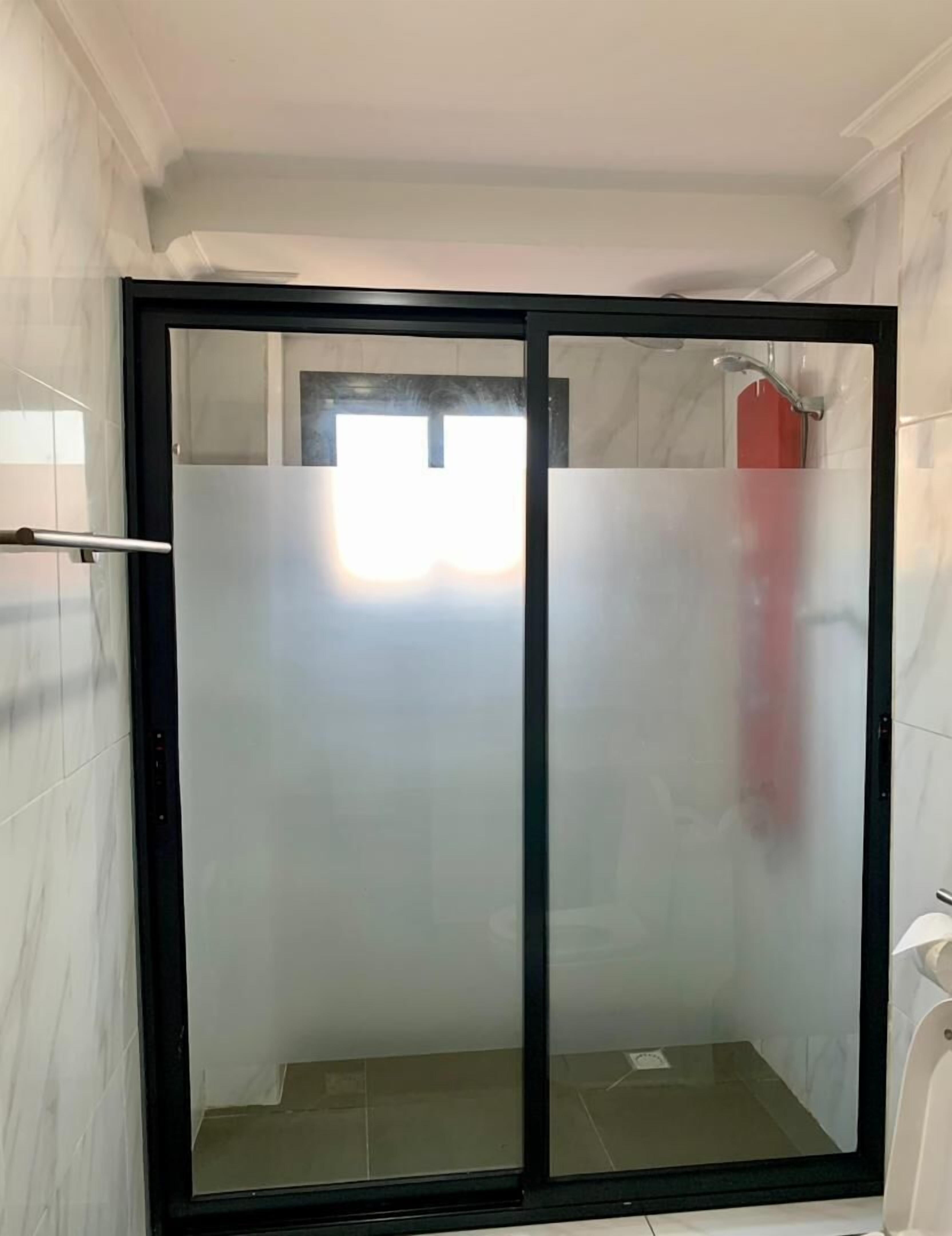 A glass-enclosed shower area with a tiled floor and a window above.