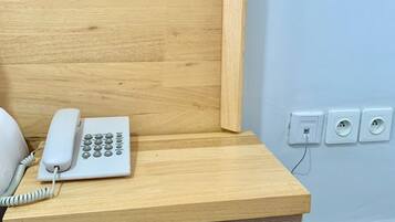 Une table de chevet en bois, avec un téléphone blanc et un tiroir doté de deux poignées.