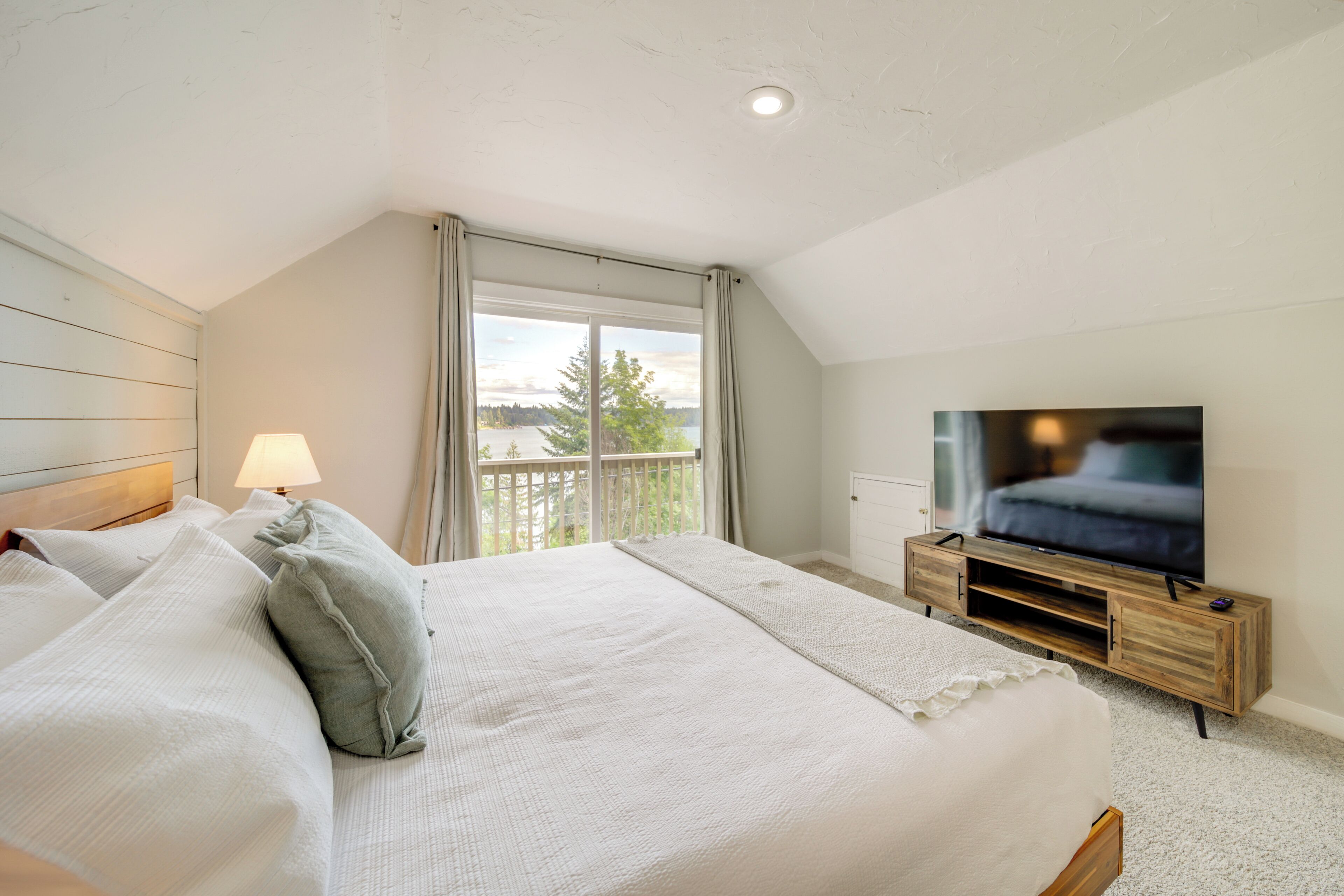 A bedroom with a large bed, a television on a wooden stand, and a window with curtains.