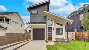 Una casa moderna de dos pisos con techo gris oscuro, un garaje amplio y un césped bien cuidado.