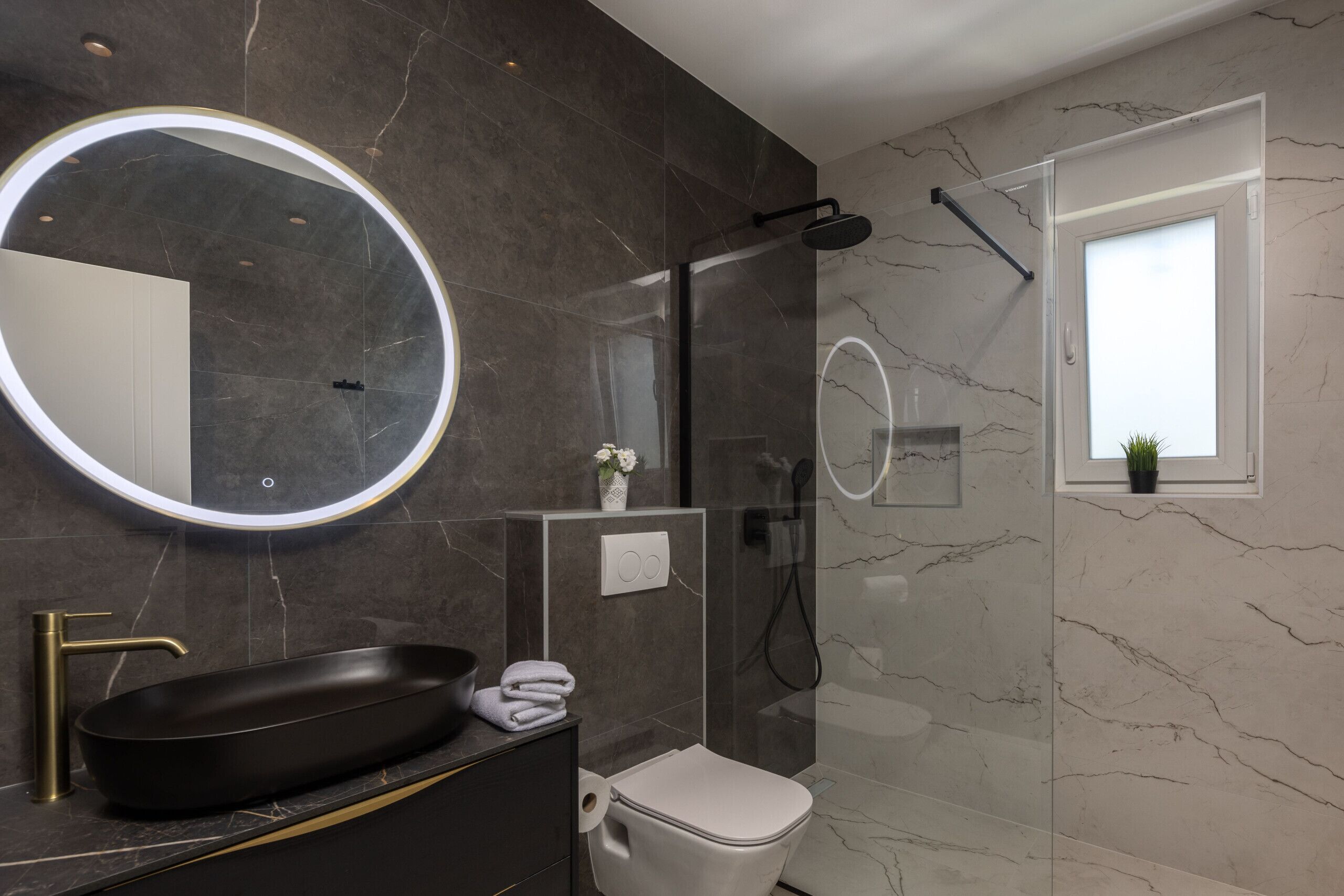 A modern bathroom with a black sink, a round mirror, a toilet, and a glass-enclosed shower.