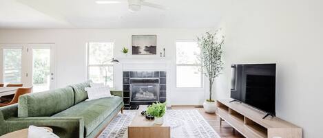 A modern living room with a green sofa, a fireplace, a television, and a ceiling fan.