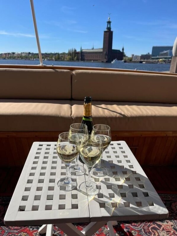A table with a bottle of champagne and four glasses on a boat deck with a cityscape view in the background. - Lilla Mälardrottningen (Stockholm)