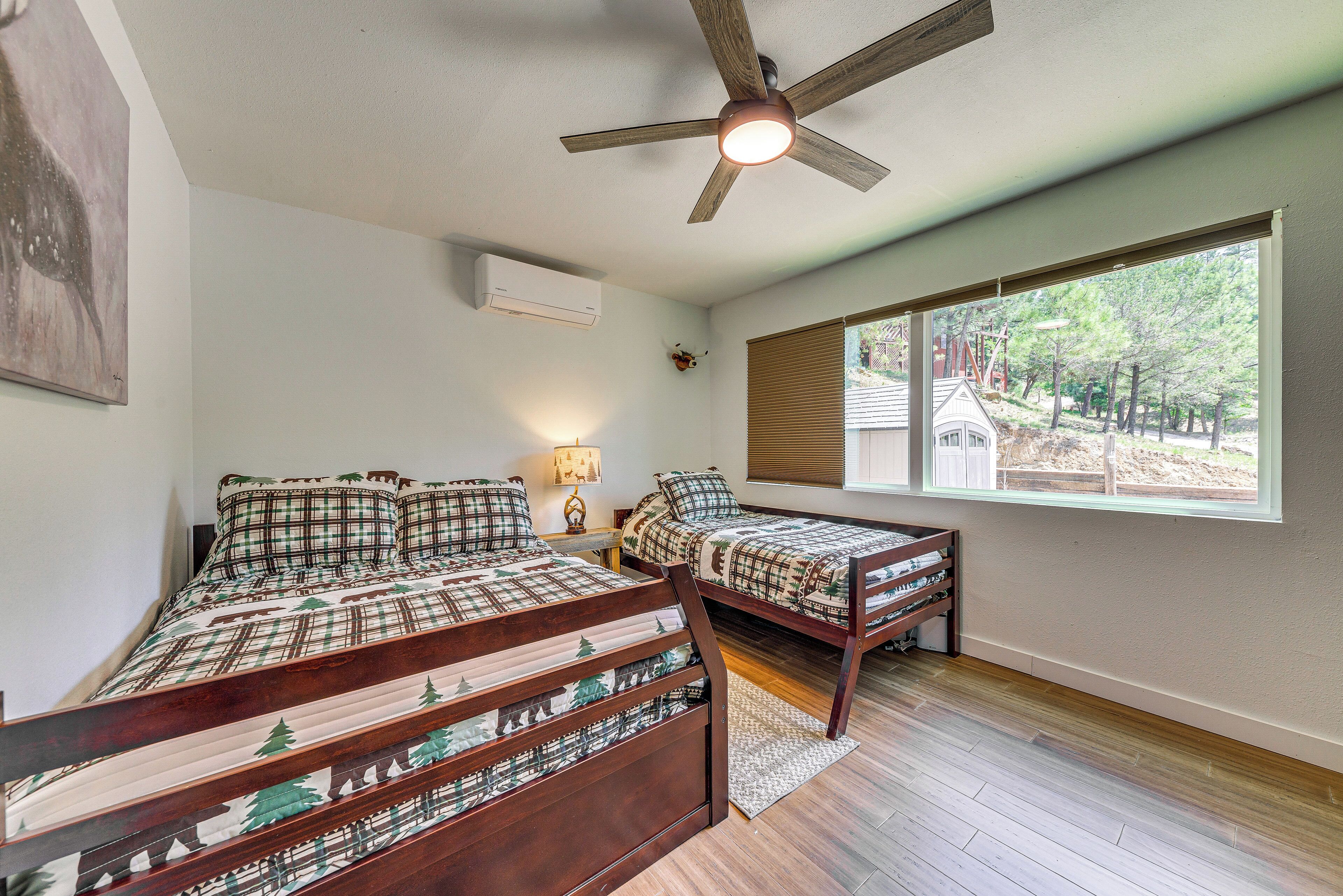 Une chambre avec deux lits, un ventilateur de plafond, une fenêtre avec des stores et une table de chevet avec une lampe.