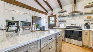 A modern kitchen with white cabinetry, a large island, stainless steel appliances, and wooden beams on the ceiling. - 4BR Ruidoso Gem: Minutes to Lake & Fun (Ruidoso)