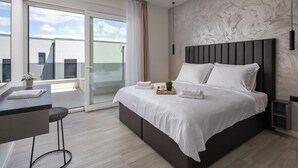 Ett modernt hotellrum med en stor säng, ett skrivbord med en stol, ett litet bord med en växt och utsikt över omgivningen.