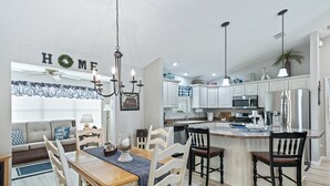 A modern kitchen with white cabinets, a central island, and a dining area with a wooden table and chairs. - Discover Your Perfect Summerhill Retreat with 2-Bed, 2-Bath, and Golf Cart! (The Villages)