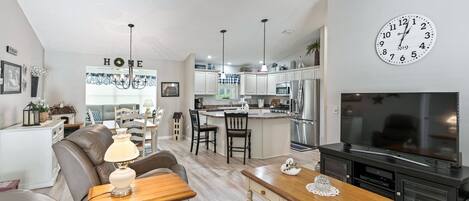 Una sala de estar moderna con sofá, mesa de centro y mueble para televisión. Cuenta con una zona de cocina con armarios y electrodomésticos.