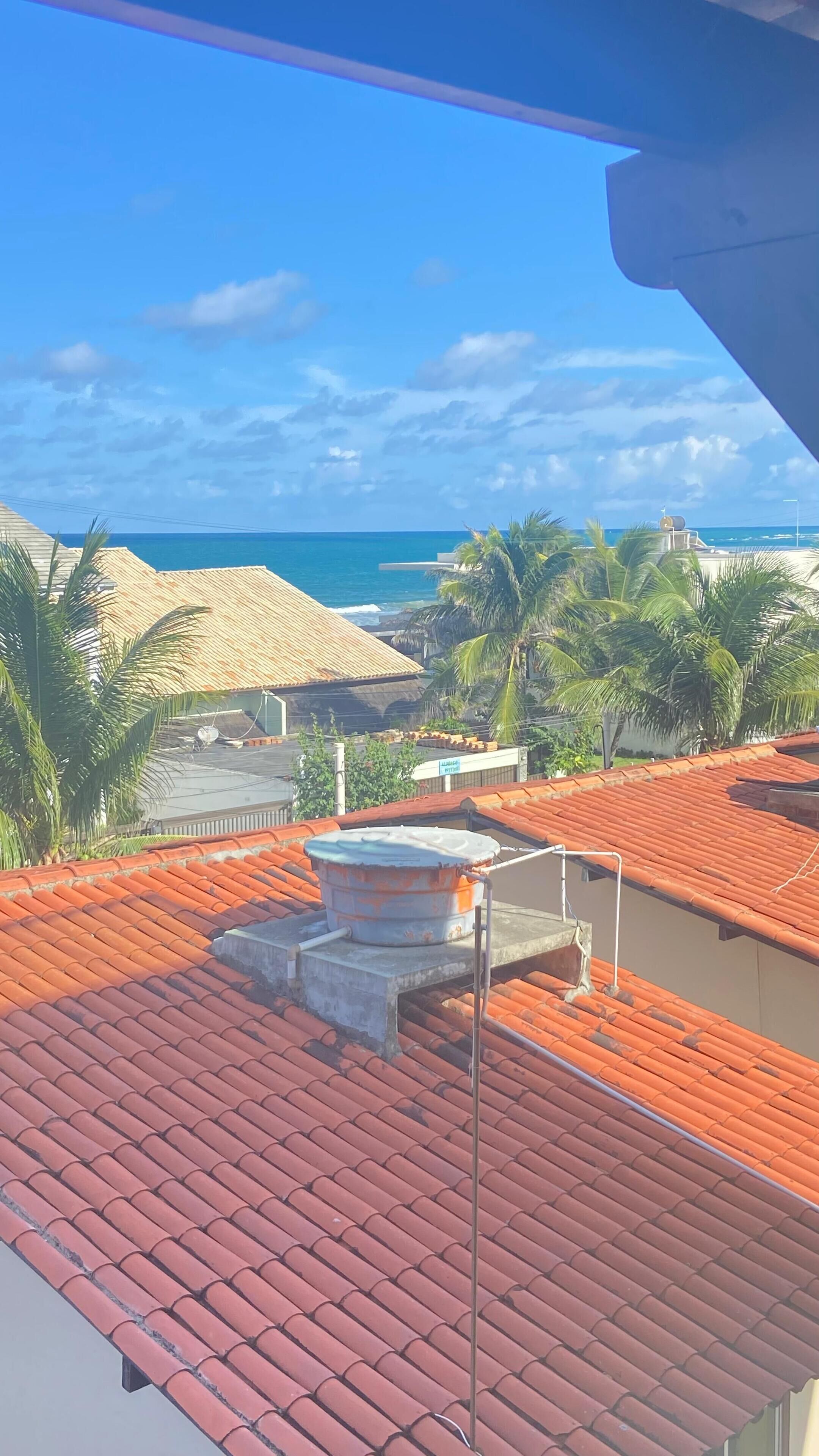 A rooftop with red tiles, a satellite dish, and a view of the ocean and palm trees.
