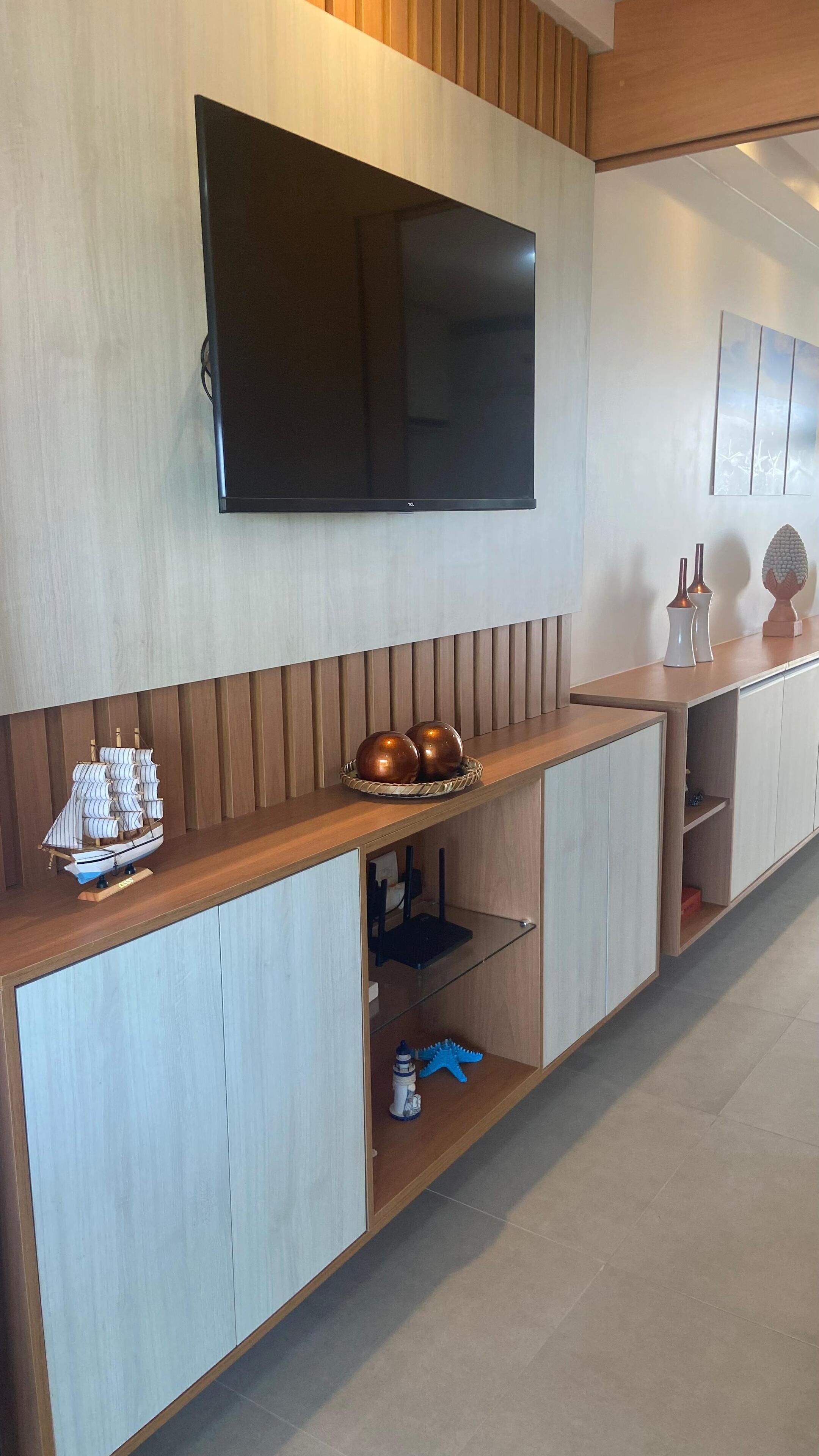 Una sala de estar moderna con un televisor de pantalla plana montado en la pared, muebles de madera y un modelo decorativo de barco.