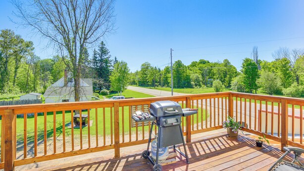 A wooden deck with a barbecue grill and a small table, overlooking a green landscape with trees and a road. - 10 Mi to Lake Superior: Eben Junction Townhome! (Eben Junction)