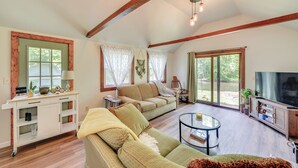 A spacious living room with a large sofa, a coffee table, and a television. There is a sliding glass door leading to a patio area. - Peaceful Hiram Retreat on Cuyahoga River! (Mantua)