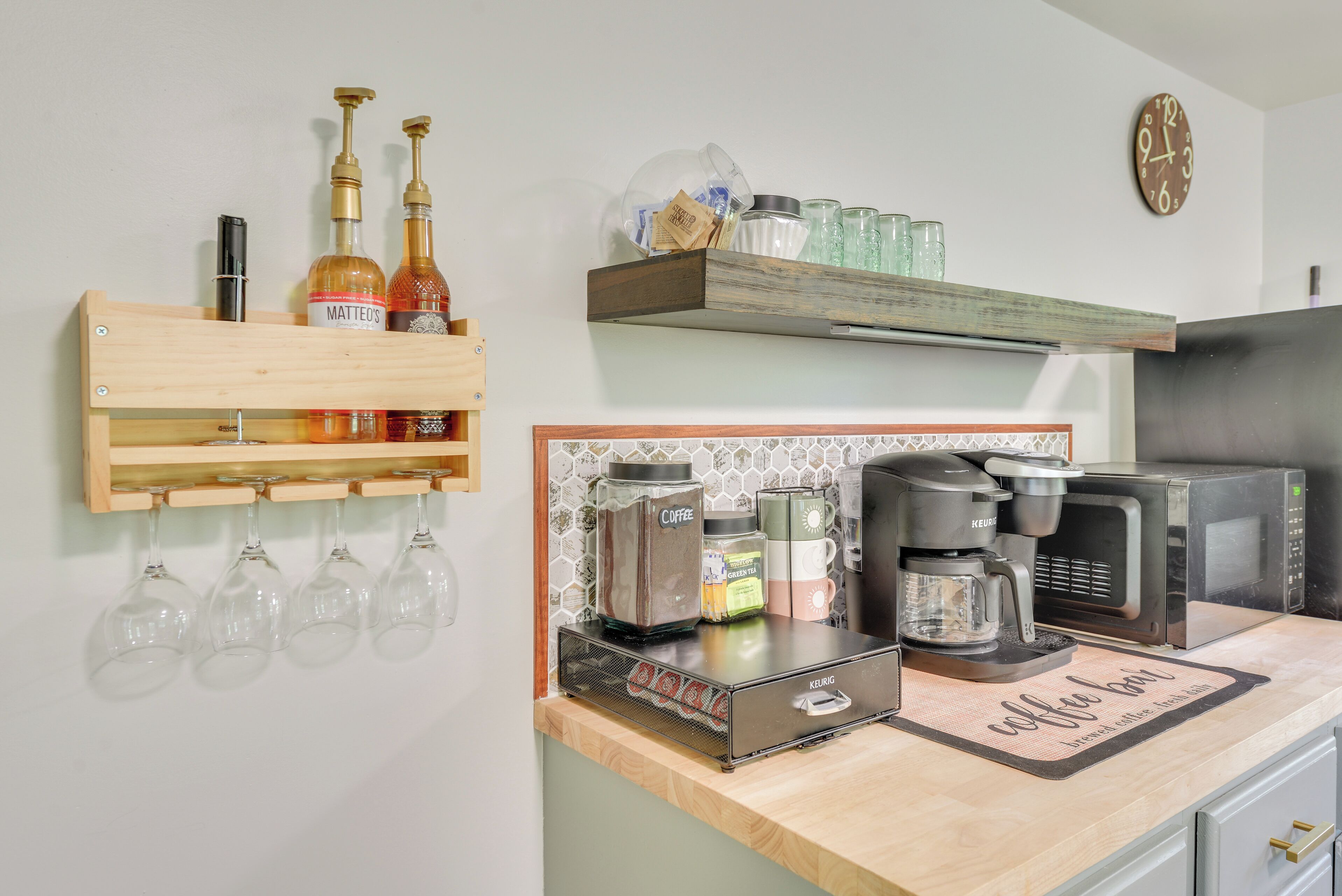 A kitchen with a coffee maker, a shelf with bottles, and a clock on the wall.