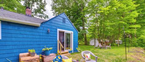 Ein blaues Haus mit Veranda, einem Tisch, zwei Stühlen und einem kleinen Garten mit Blumen.