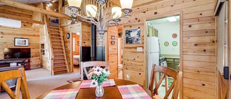 A wooden cabin interior with a dining area featuring a wooden table, chairs, and a chandelier.