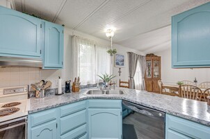 Cocina con armarios azul claro, encimera de granito, lavavajillas y mesa de comedor de madera con sillas.