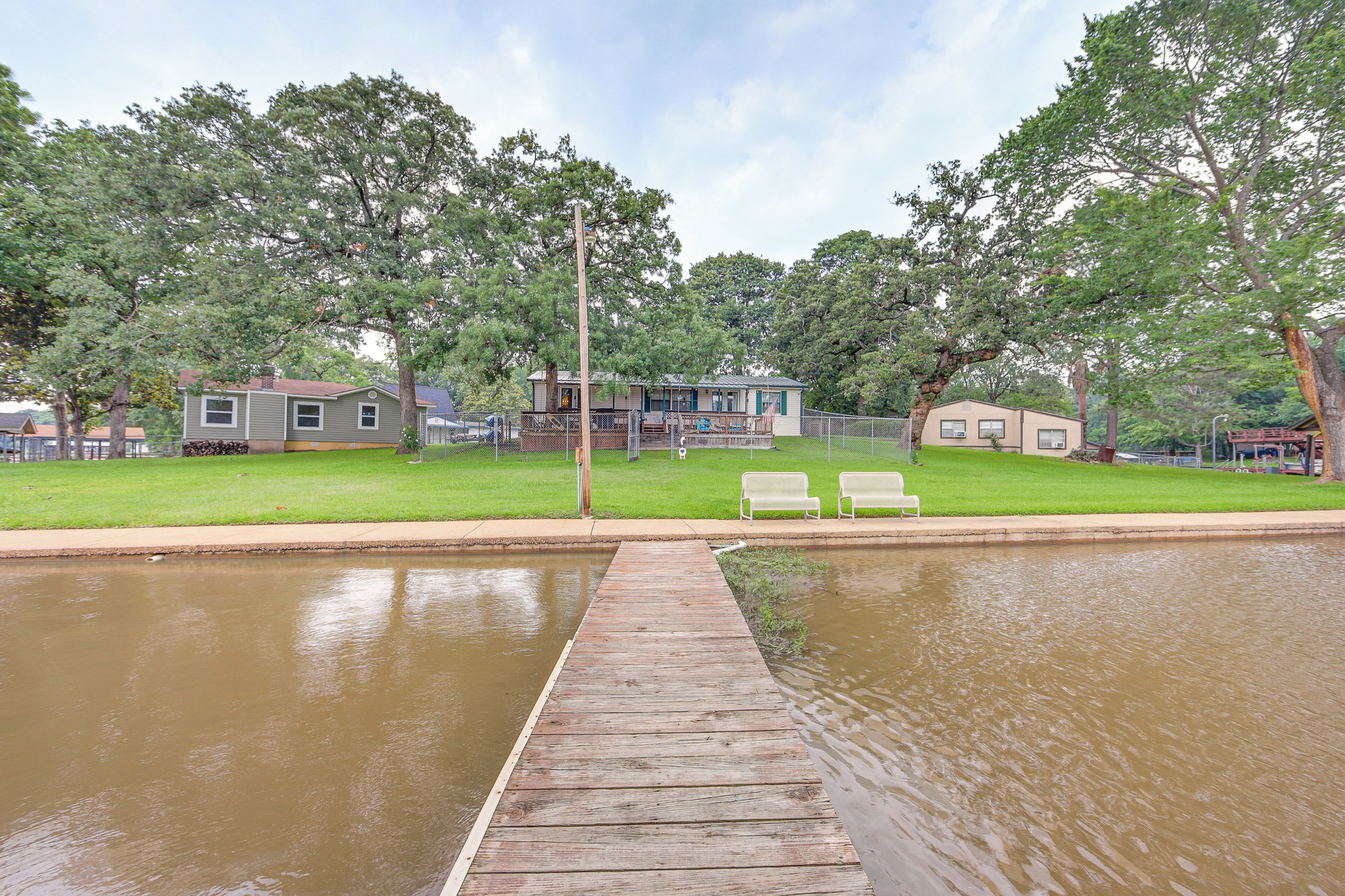 A wooden dock leading to a calm water body, surrounded by green lawns and trees.