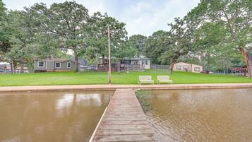 A wooden dock leading to a calm water body, surrounded by green lawns and trees.