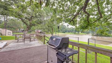 A wooden deck with a grill, outdoor furniture, and a view of a river.