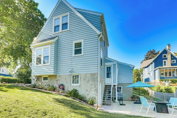 A two-story house with a sloped roof, a covered patio with outdoor furniture, and a well-maintained lawn. - Charming Lake Mills Home Near Rock Lake & Beach (Lake Mills)