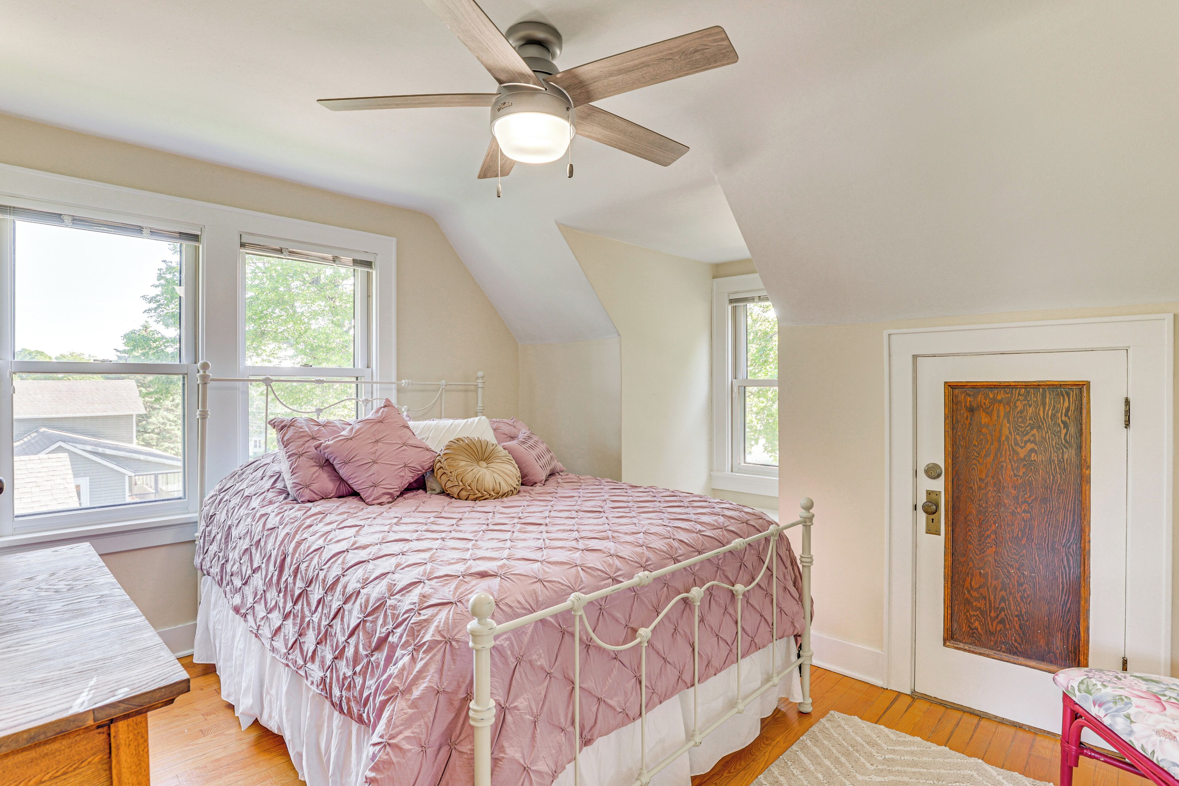 A bedroom with a bed, a ceiling fan, a door, and windows.