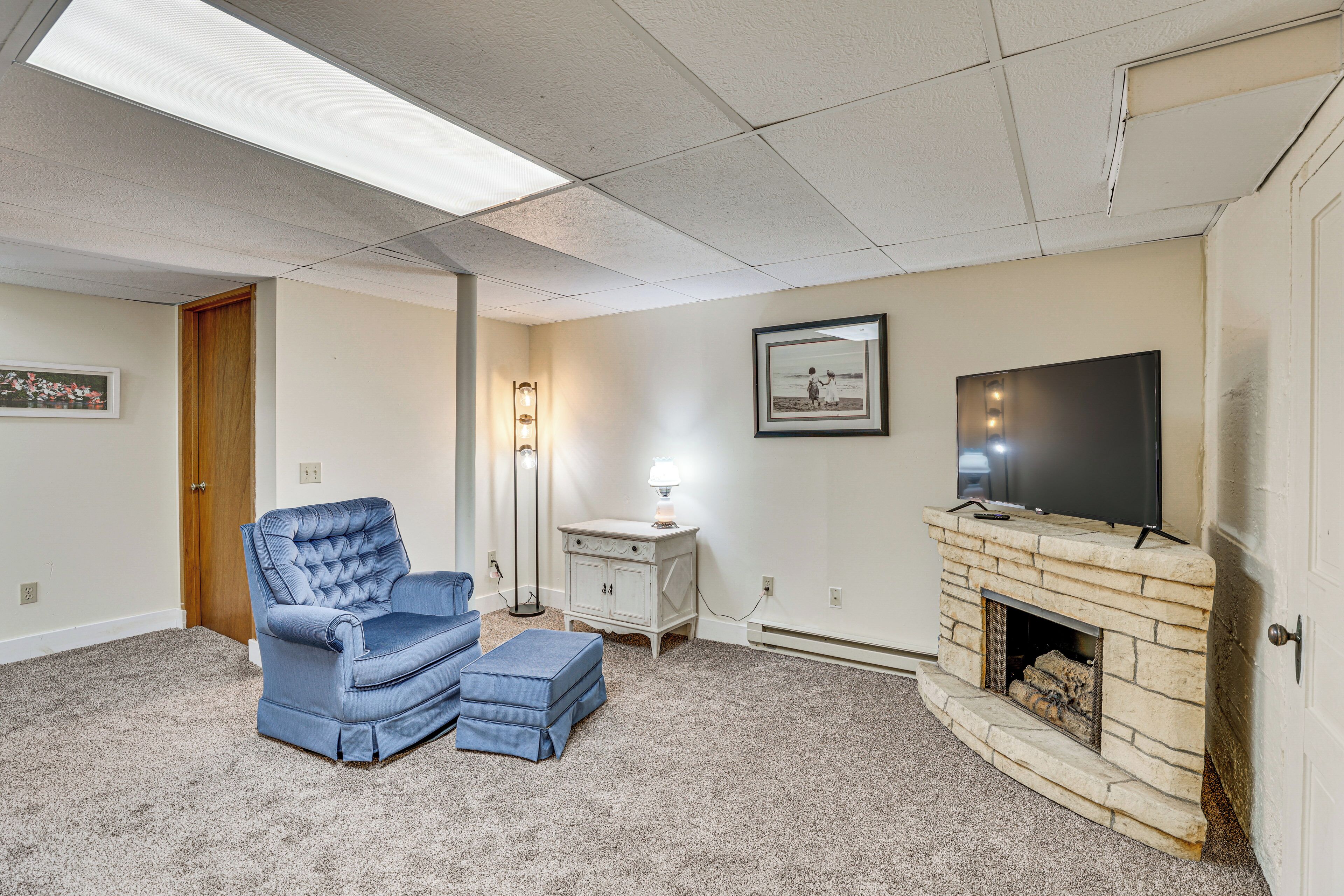 A living room with a blue armchair, a white side table with a lamp, a fireplace, and a television on the wall.