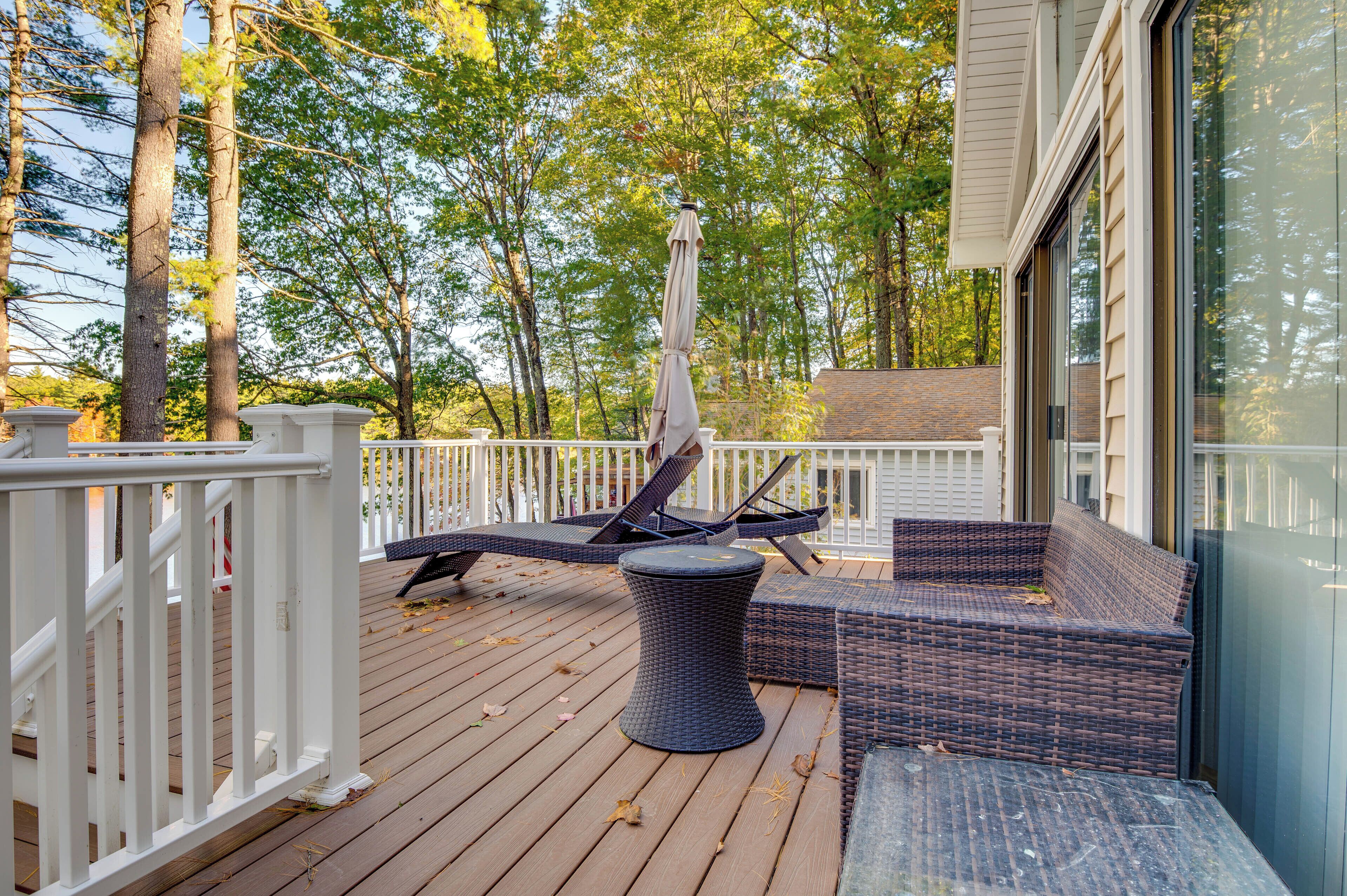 A wooden deck with wicker furniture, including a sofa and a table, and a white railing.