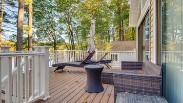 A wooden deck with wicker furniture, including a sofa and a table, and a white railing.