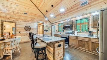 A wooden cabin interior with a kitchen, dining area, and bar stools.