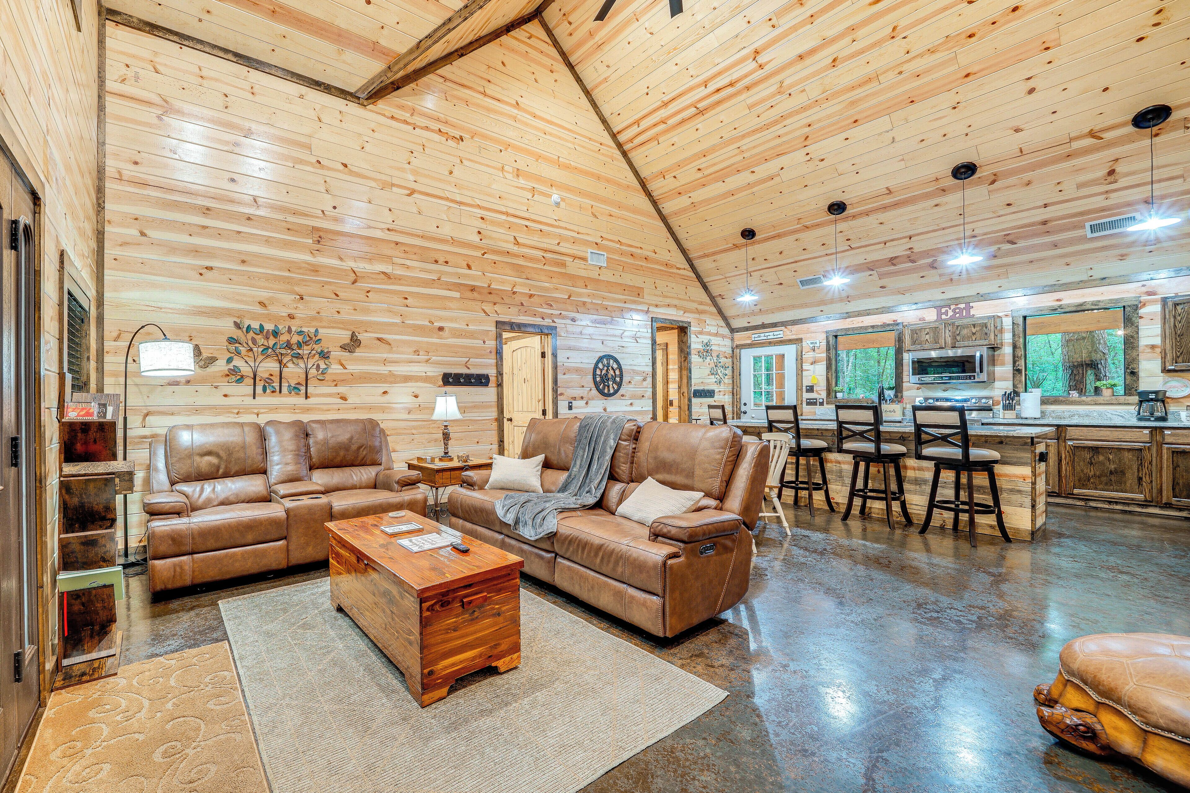 A spacious living area with a leather sofa, a wooden coffee table, and a kitchen area with a microwave and bar stools.
