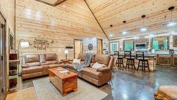 A spacious living area with a leather sofa, a wooden coffee table, and a kitchen area with a microwave and bar stools.