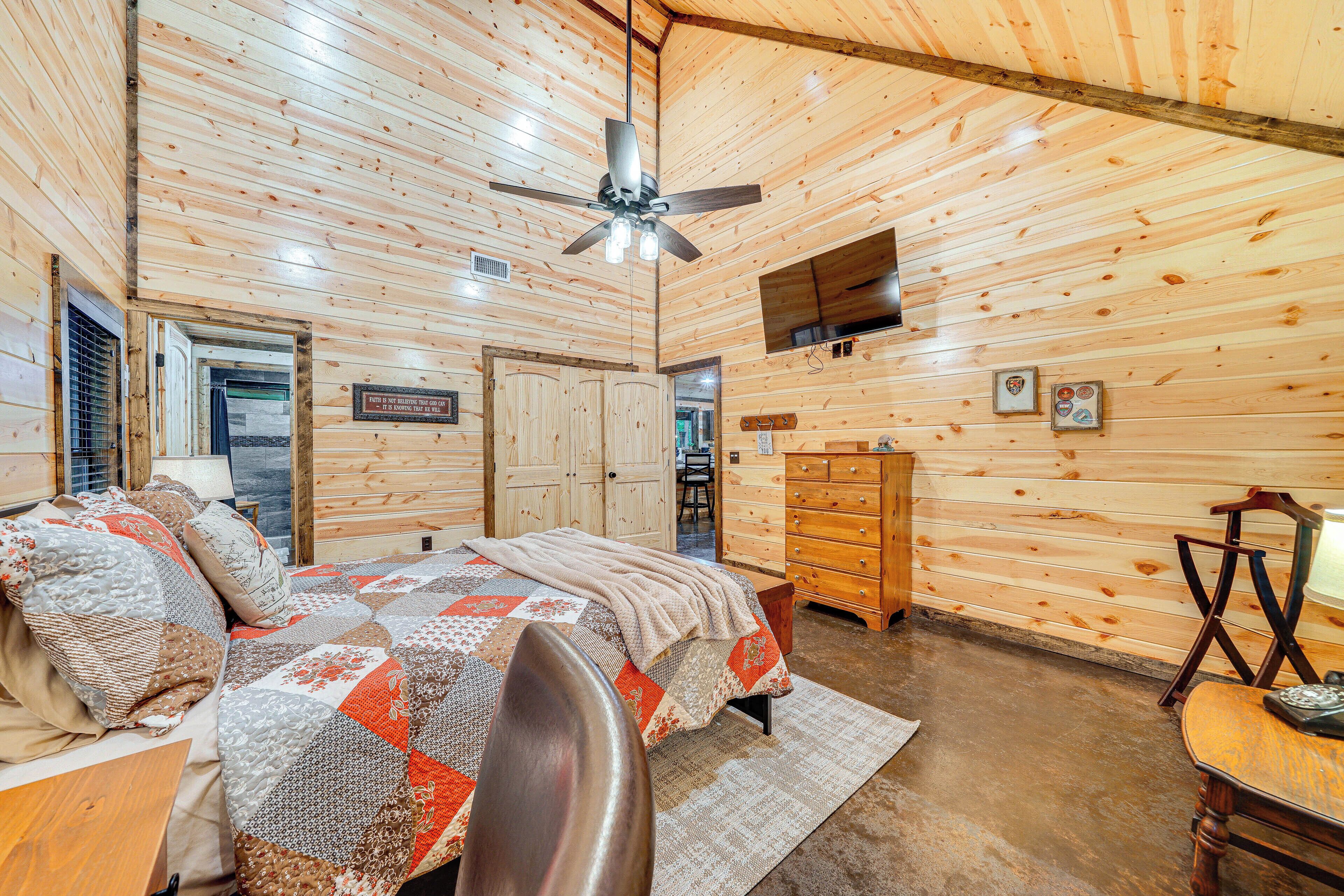 A wooden cabin interior with a bed, dresser, and ceiling fan.