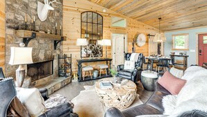 L’intérieur d’un chalet confortable, avec des murs en rondins de bois, une cheminée en pierre, des meubles en cuir et un coin repas.