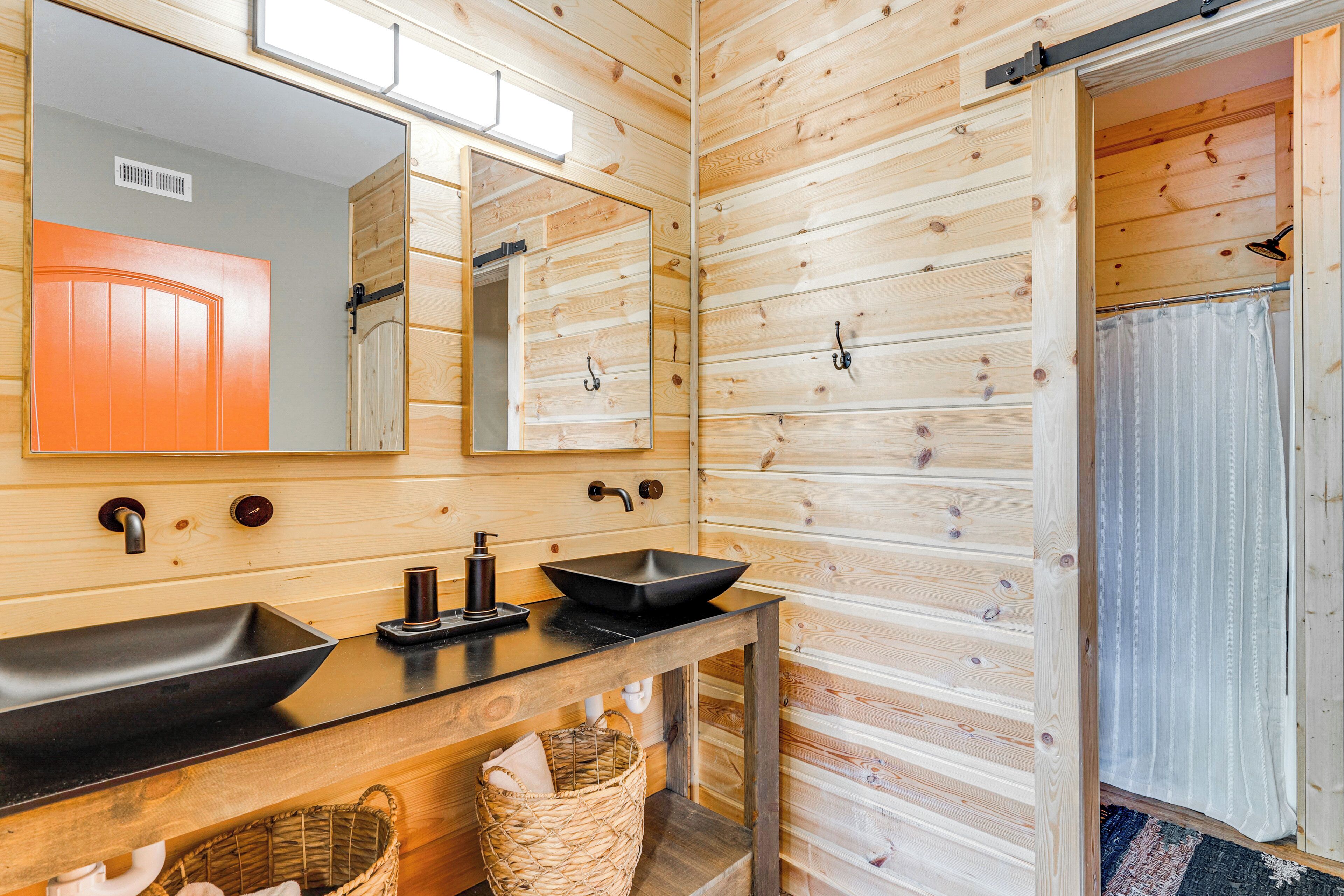 A wooden cabin bathroom with a large mirror, two sinks, a towel rack, and a shower curtain.