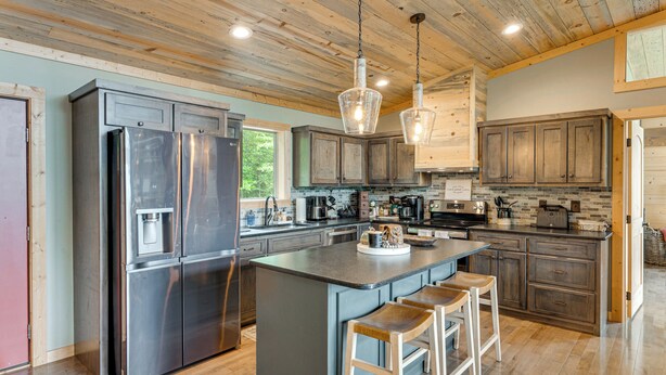 Une cuisine moderne dotée d’un grand îlot central, d’appareils électroménagers en acier inoxydable, de meubles en bois et de luminaires suspendus.