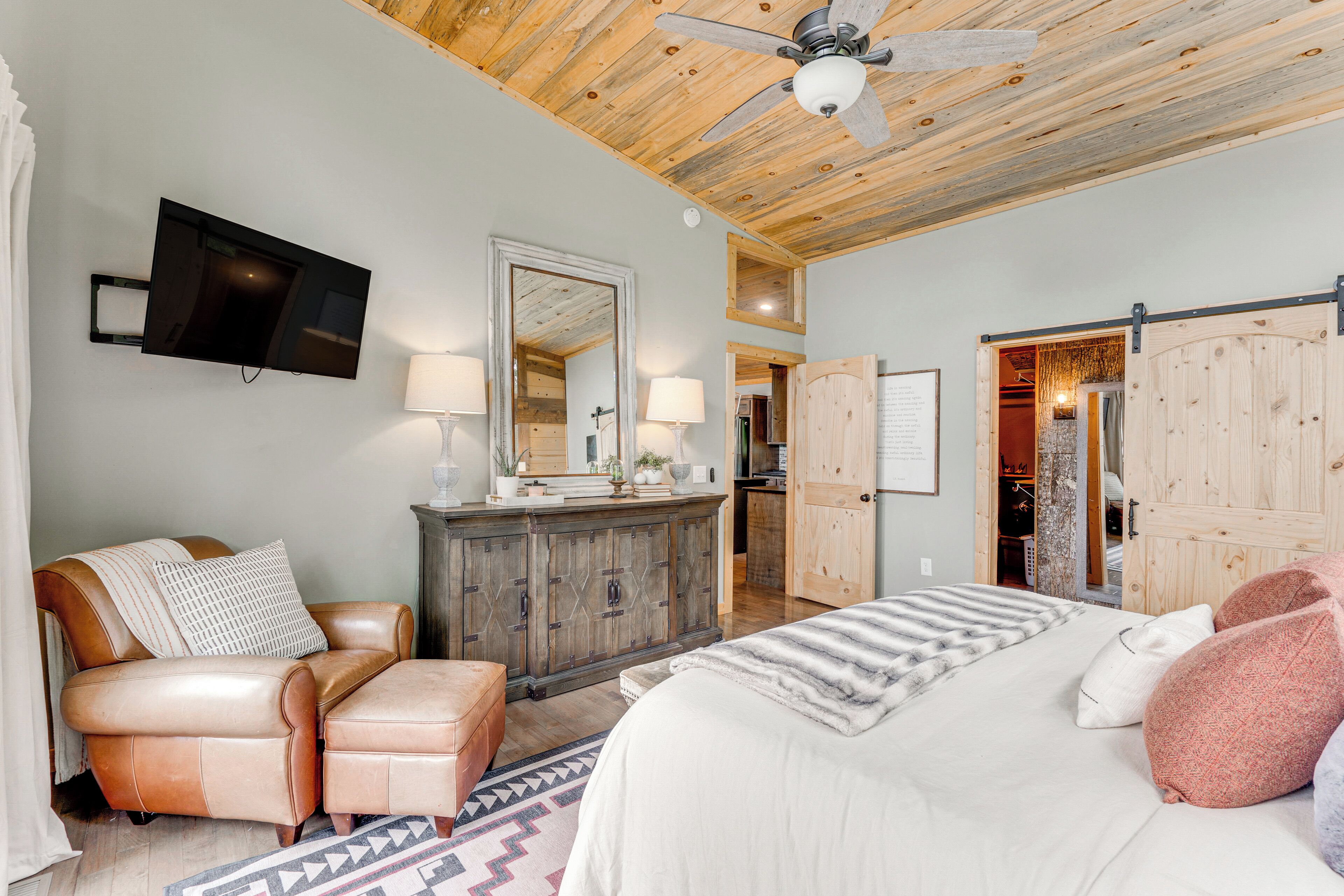A bedroom with a bed, a leather sofa, a wooden cabinet, and a television mounted on the wall.
