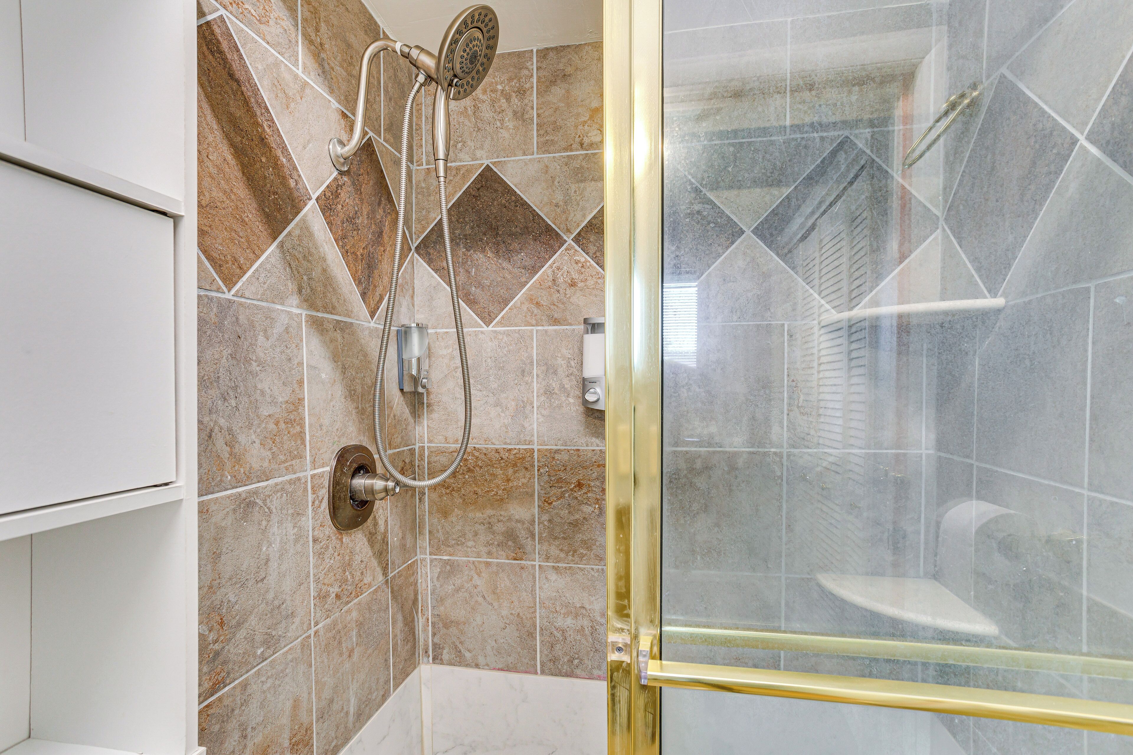 Une douche avec une porte en verre, une douchette à main et un panneau de commande fixé au mur.